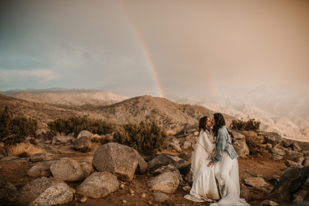 Couple kissing during their elopement in Minnesota with a double rainbow behind them.