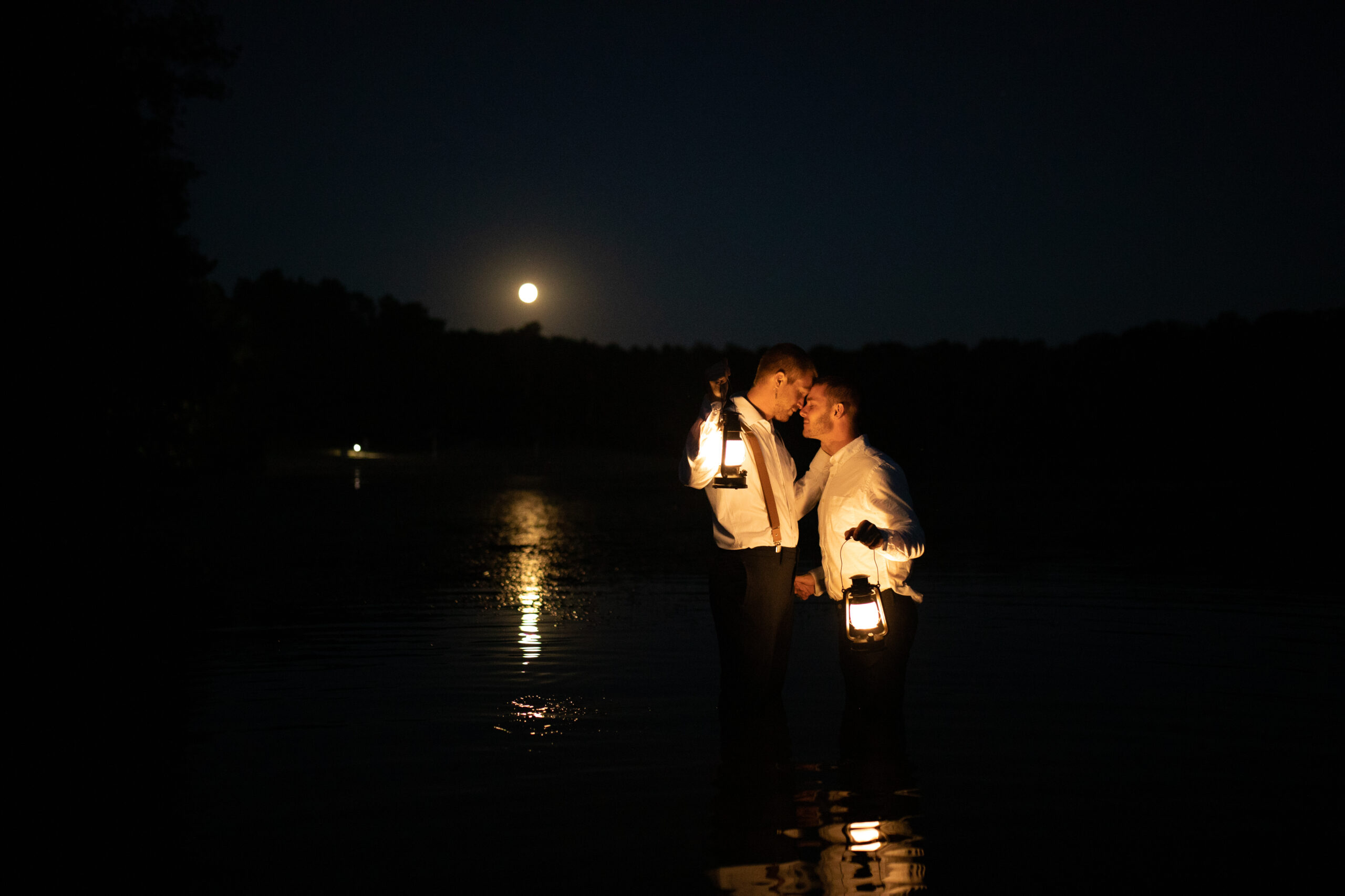 LGBTQ+ couple posing in the water with lanterns during their elopement shoot.
