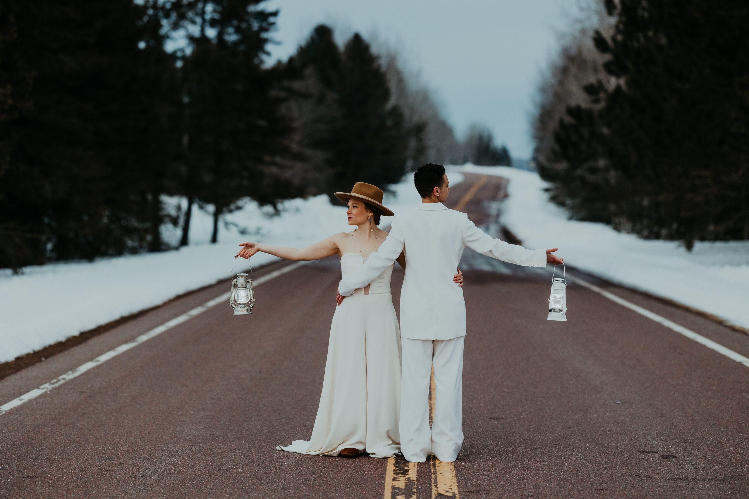 LGBTQ+ couple posing in the middle of a forested road with lanterns.