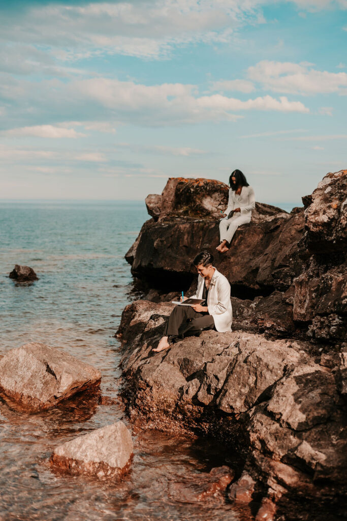 Eloping couple writing vows on some rocks near a beach.