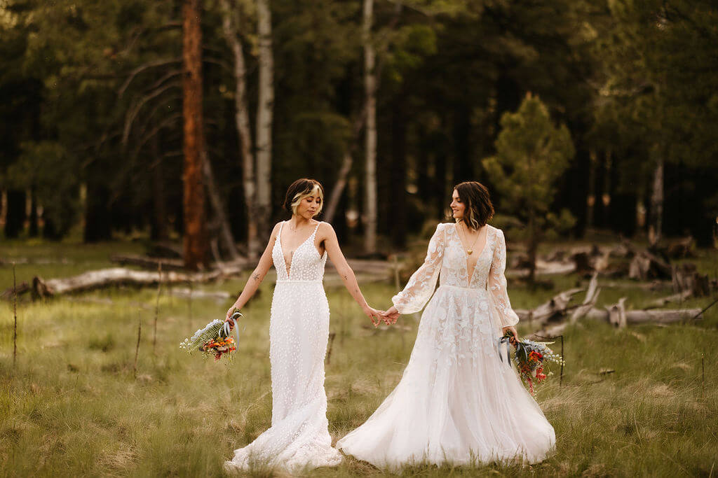 Couple outdoors in their wedding dresses holding hands.