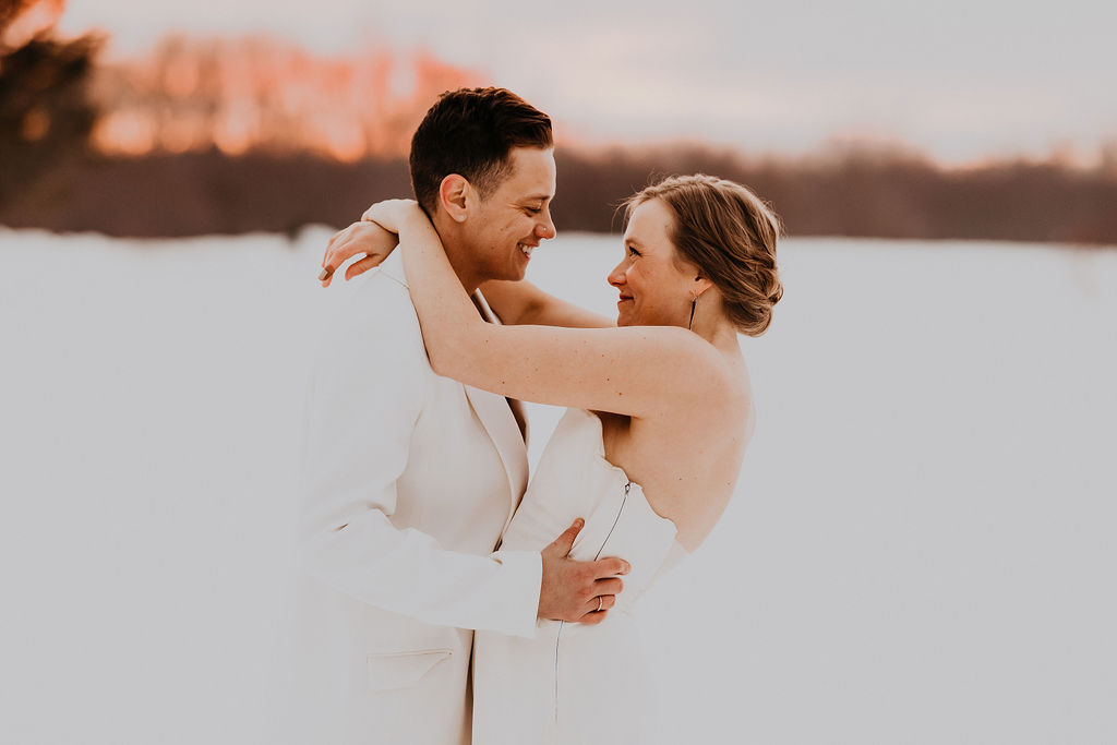 Couple holding each other during their wedding. They are wearing all white with a winter backdrop.